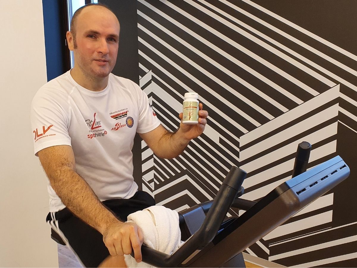 Gianluca su una cyclette TechnoGym in palestra che pedala sudato con in mano una confezione di Munogen
