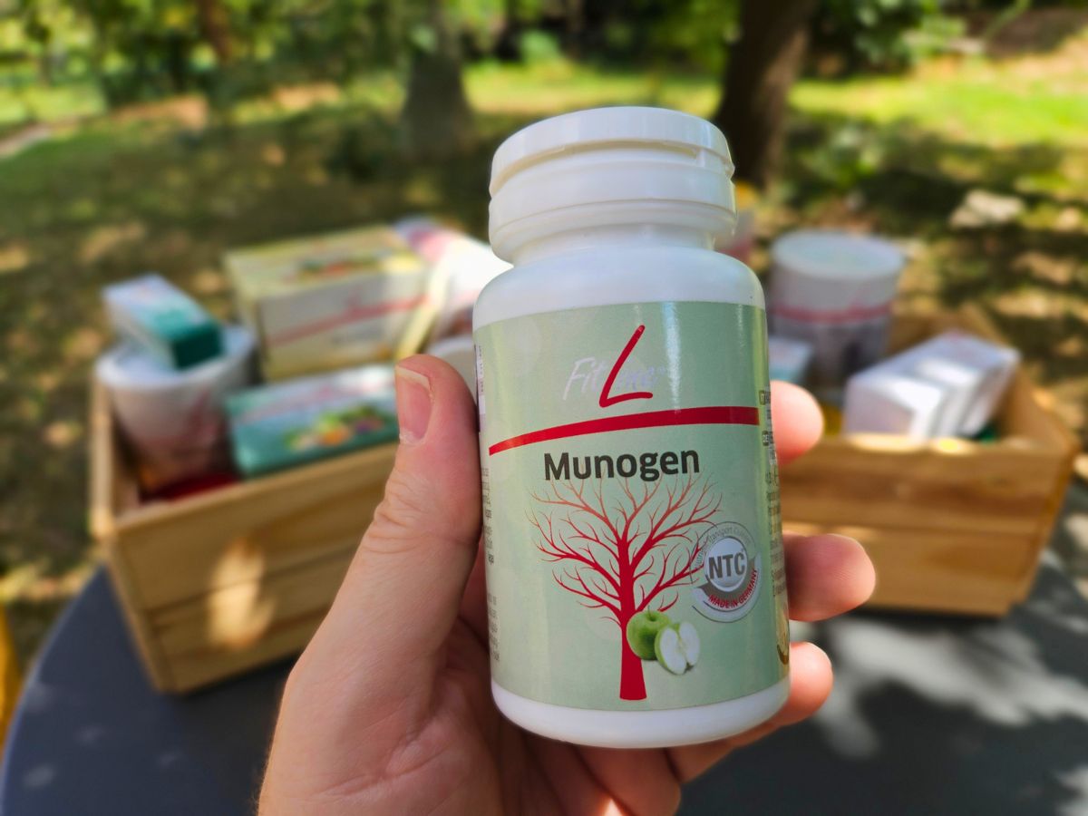 Mano che tiene confezione di Munogen e pacco FitLine con altri prodotti sfocati sullo sfondo