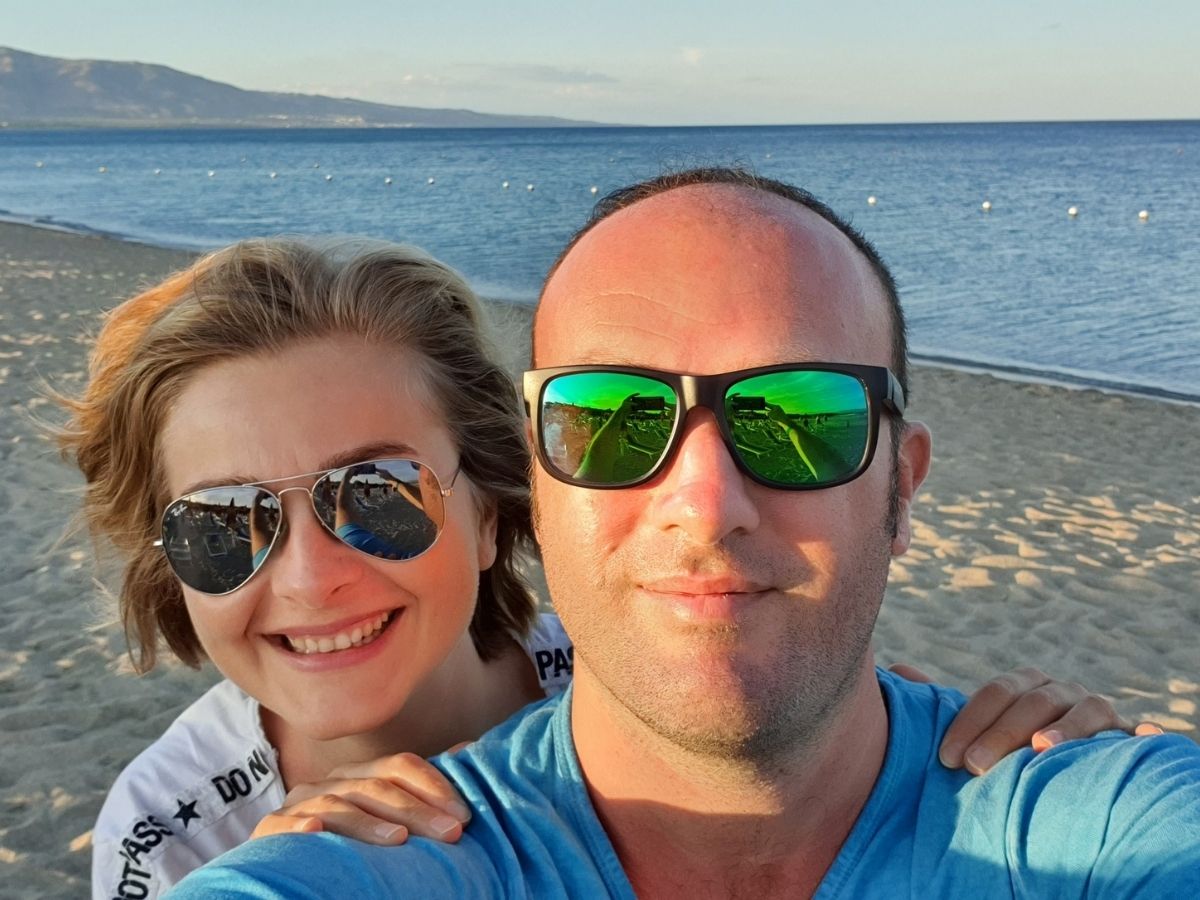 Simonetta e Gianluca con gli occhiali da sole abbracciati in spiaggia con il mare calmo al tramonto