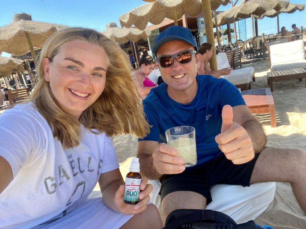 Heart Duo FitLine: Simonetta e Gianluca fanno un selfie al mare sotto l'ombrellone con un flacone di Heart Duo in mano e un bicchiere di prodotto pronto da bere